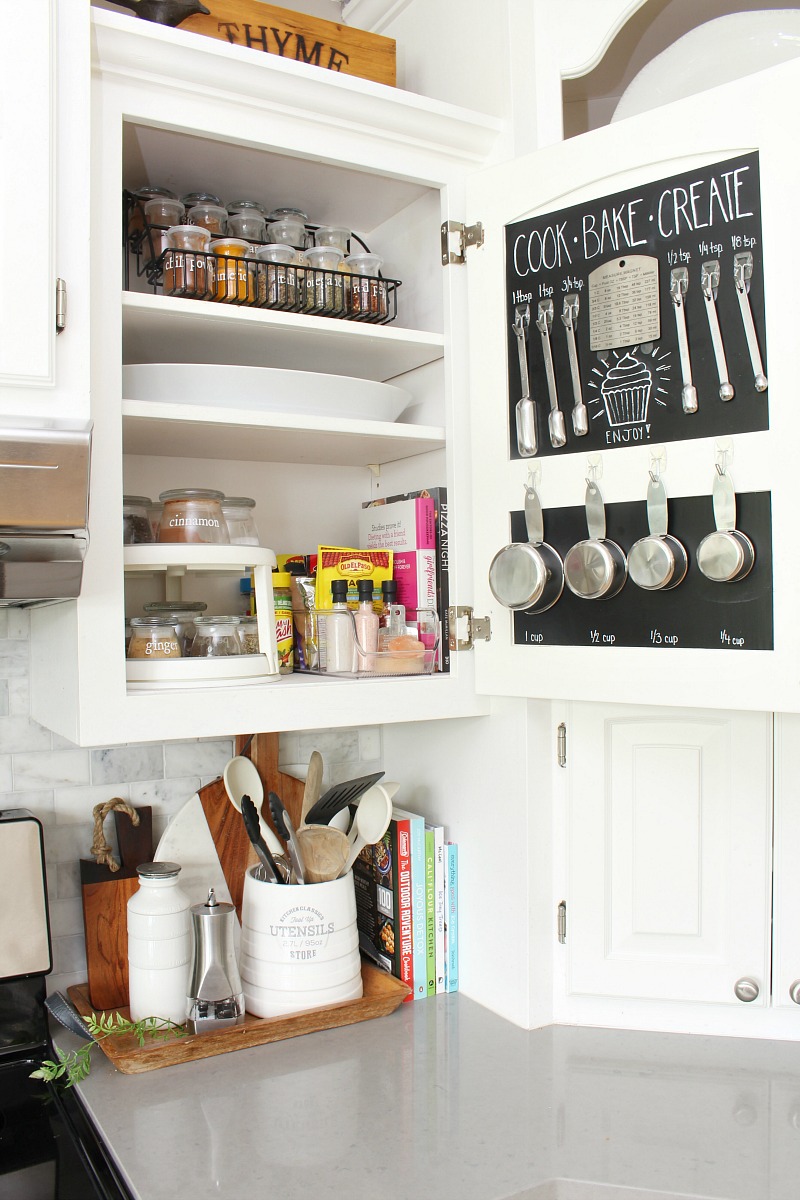 Kitchen cabinet using the inside of the cabinet door to store measuring cups and spoons.