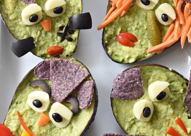 Guacamole monsters in an avocado decorated with a variety of vegetables.