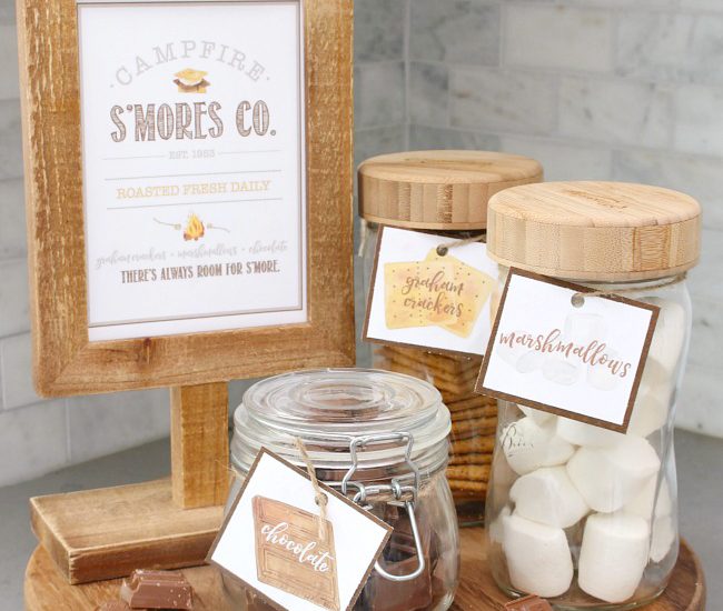 Campfire S'mores Printable in a wooden frame with s'mores ingredients in labeled mason jars.