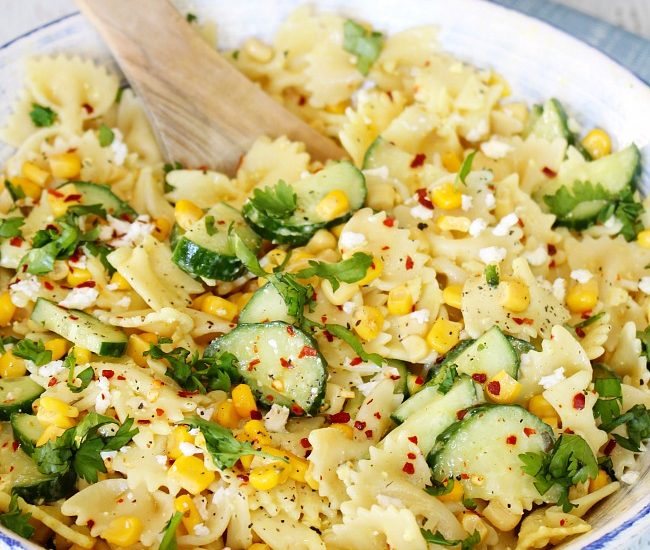 Cucumber and sweet corn salad in a white bowl with wood serving spoon.