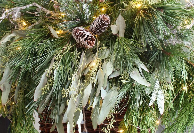 Christmas basket wreath with fresh greenery and fairy lights.