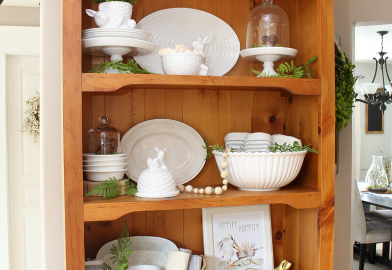 Wood hutch decorated for Easter with white dishes and Easter bunnies.