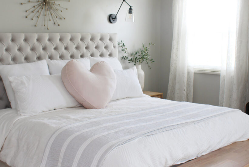 Grey upholstered bed with white bedding and a heart pillow.