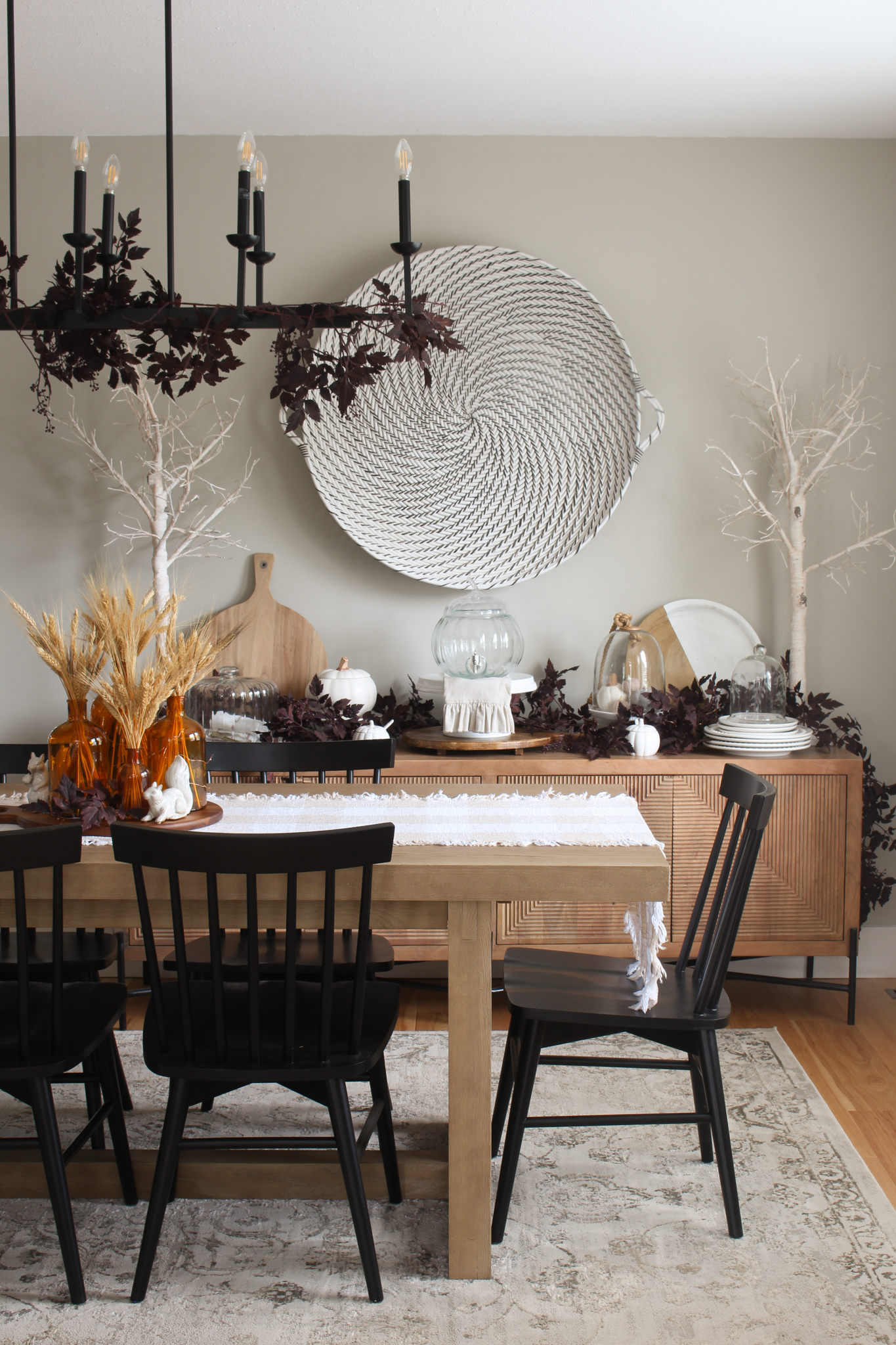 Modern dining room with wood table and side board with black chairs. Simple fall decor with wheat and plum cimicifuga garlands and branches.