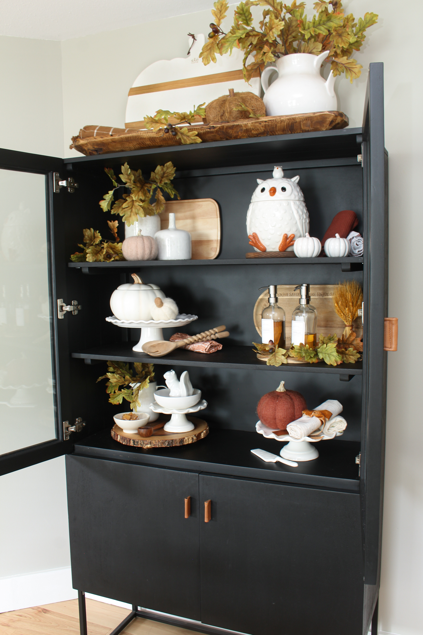 Modern black bar cabinet decorated for fall with neutral pieces, pumpkins and oak leaves.