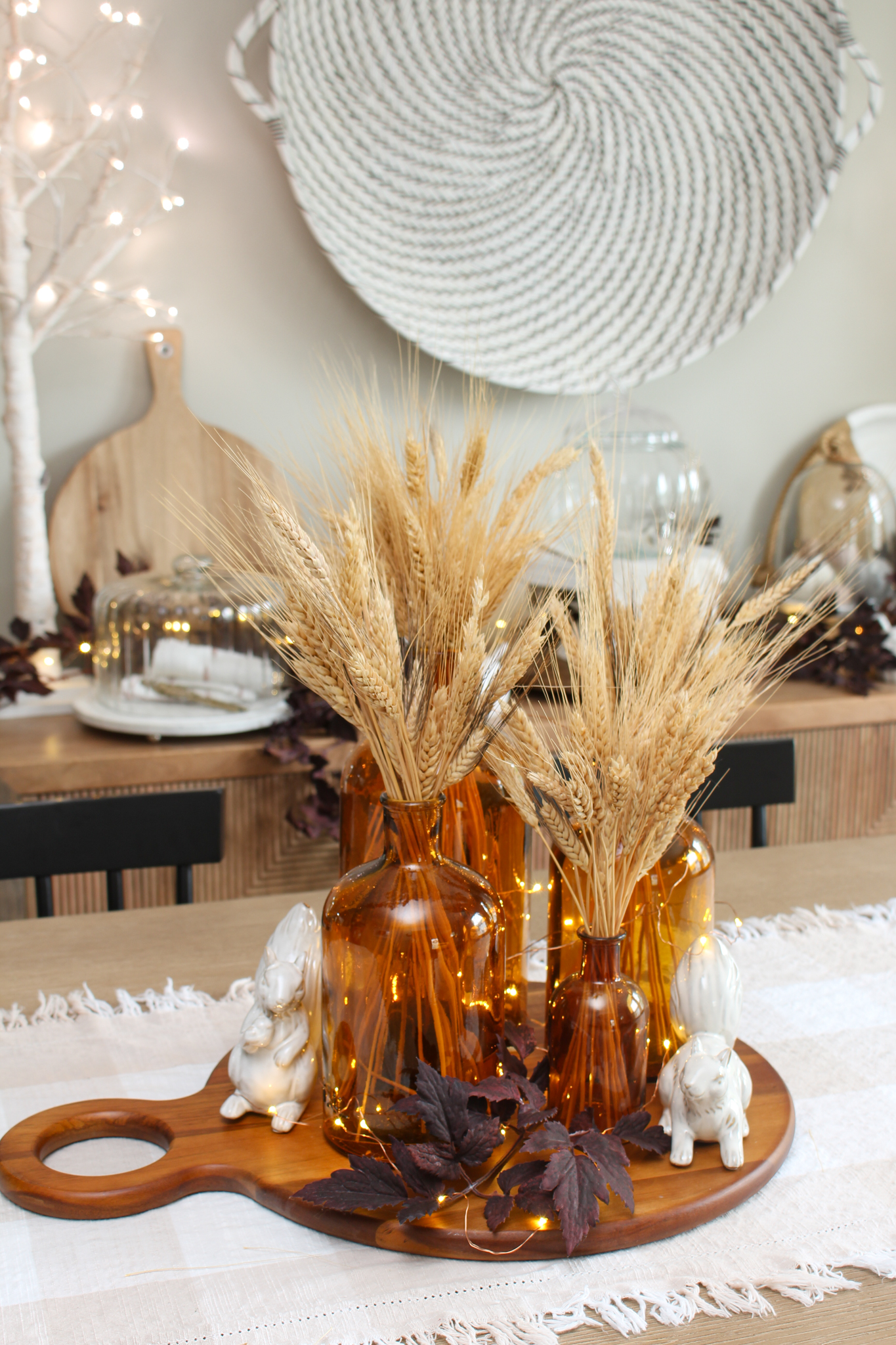 Collection of amber glass bottles filled with wheat and twinkle lights on a wood tray.