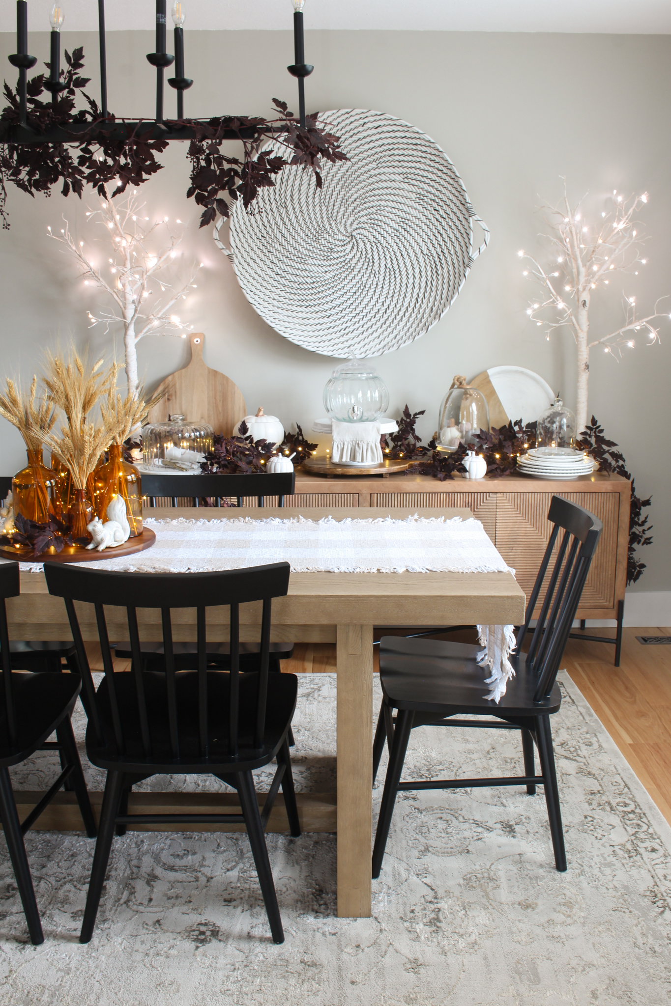 Modern dining room with wood table and side board with black chairs. Simple fall decor with wheat and plum cimicifuga garlands and branches.