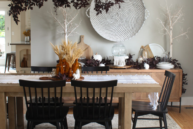 Modern dining room with wood table and side board with black chairs. Simple fall decor with wheat and plum cimicifuga garlands and branches.