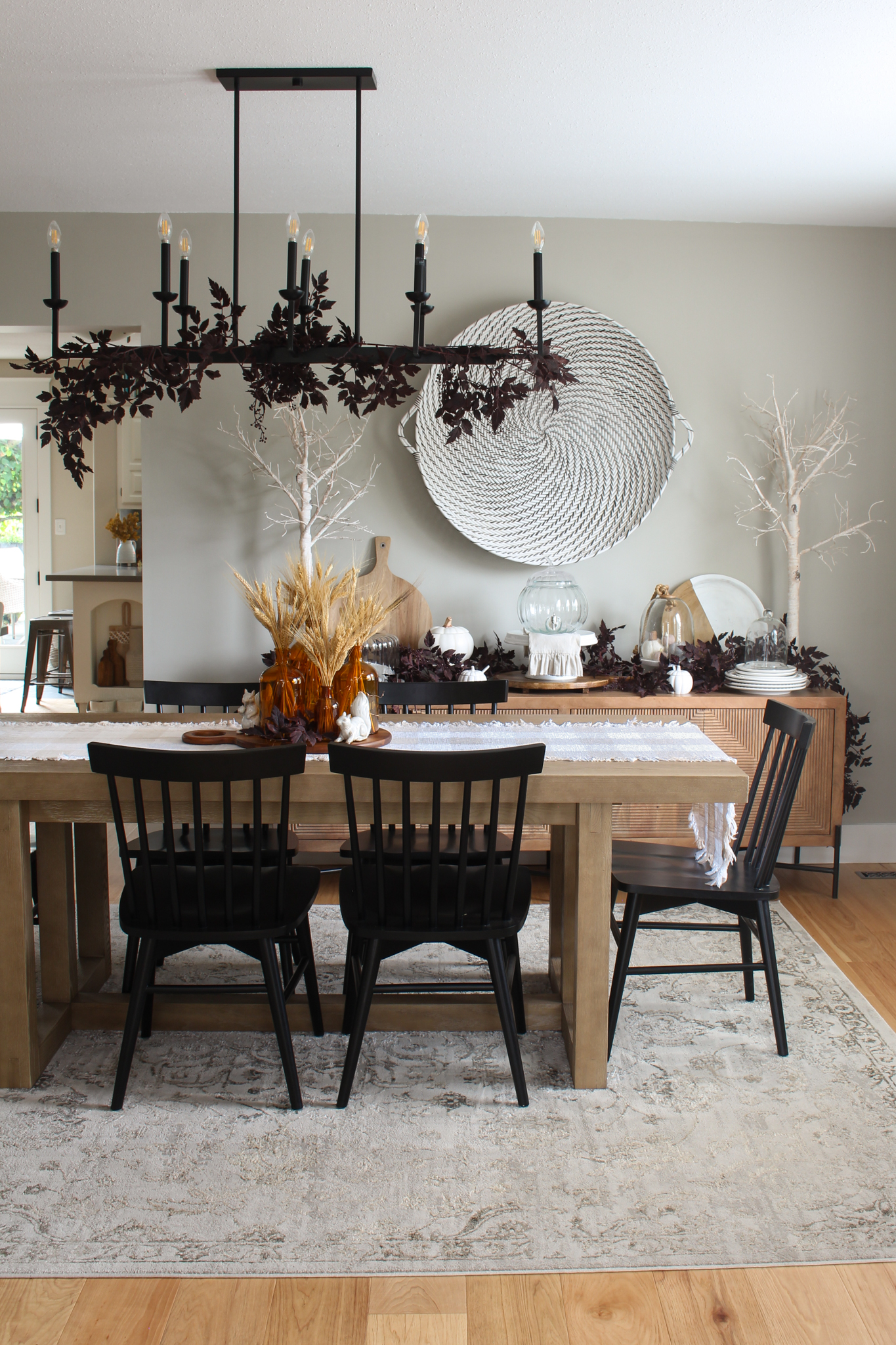 Modern dining room with wood table and side board with black chairs. Simple fall decor with wheat and plum cimicifuga garlands and branches.