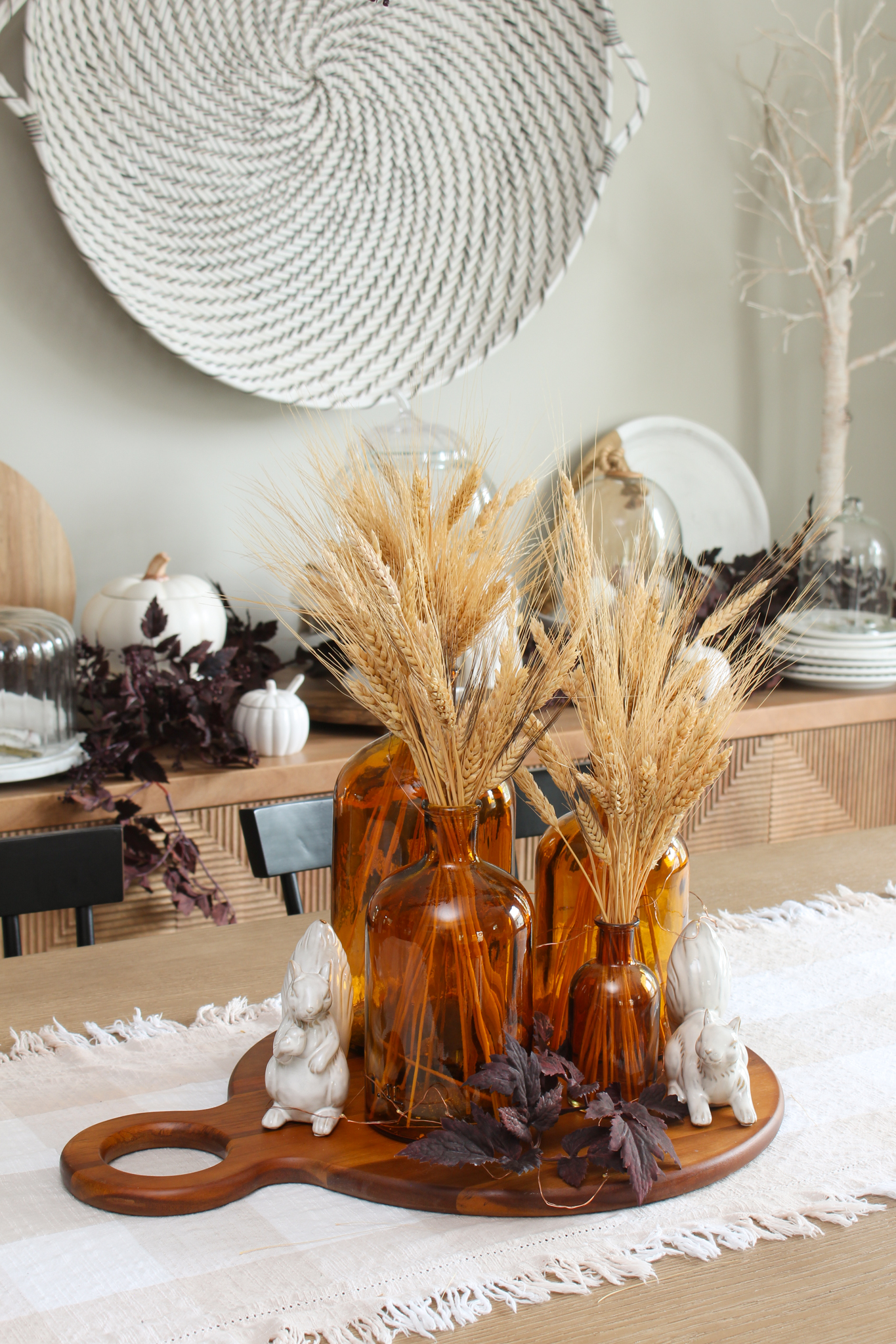 Collection of amber glass bottles filled with wheat and twinkle lights on a wood tray.