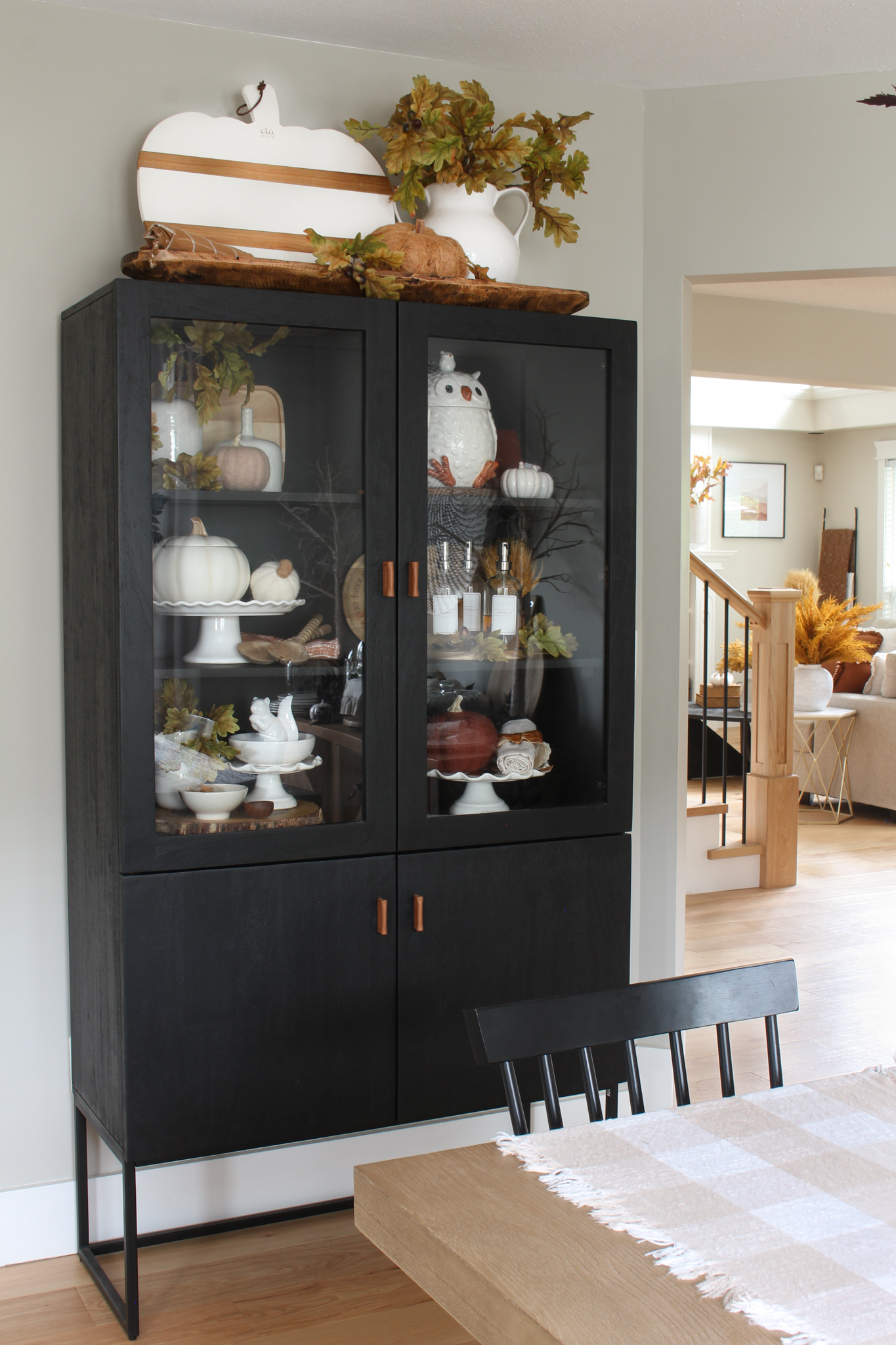 Modern fall dining room with black bar cabinet decorated for fall with neutral pieces, pumpkins and oak leaves.