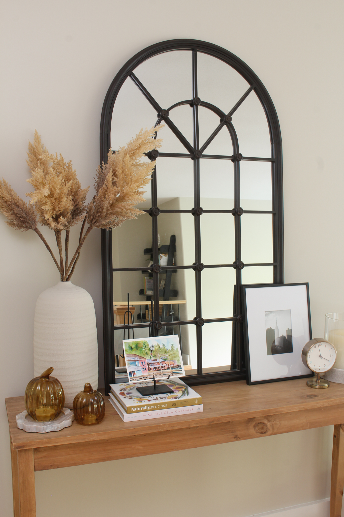 Hallway table with black mirror and vase with faux pampas grass and light up pumpkins.