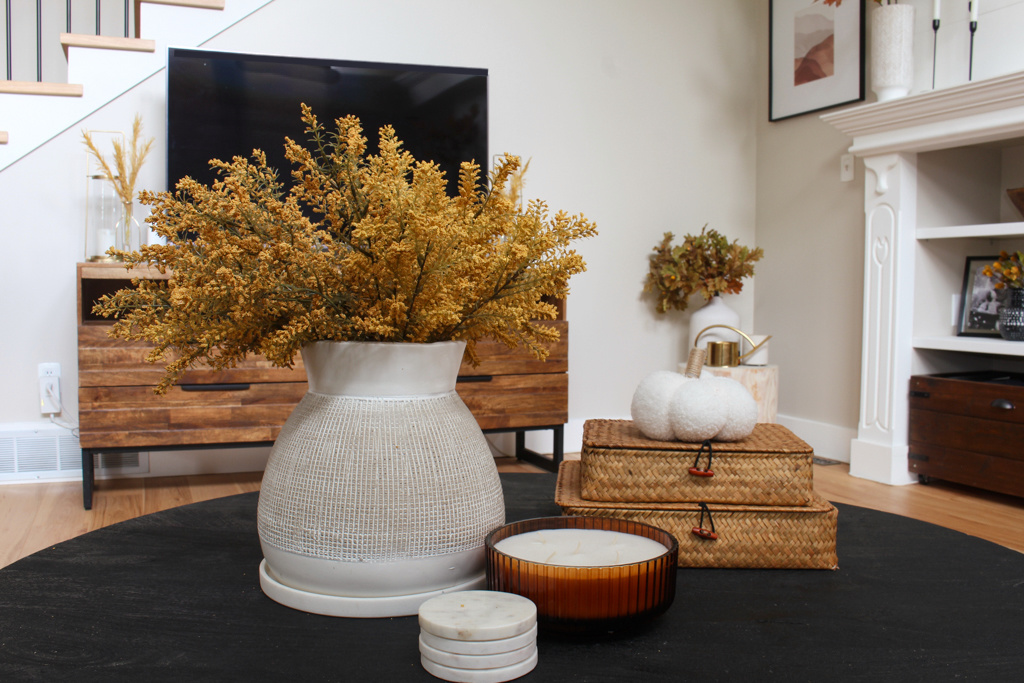 Coffee table decorated for fall with a vase with fall florals, wicker baskets and a fall candle.