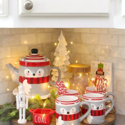 Kitchen tray decorated for Christmas with a raccoon mug and teapot set and Christmas lights.