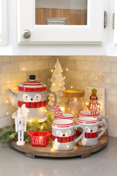 Kitchen tray decorated for Christmas with a raccoon mug and teapot set and Christmas lights.