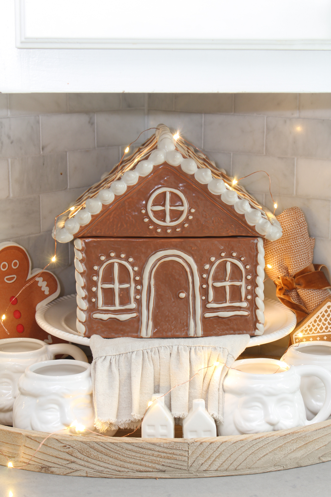 Gingerbread house cookie jar on a cake stand with twinkle lights around it.