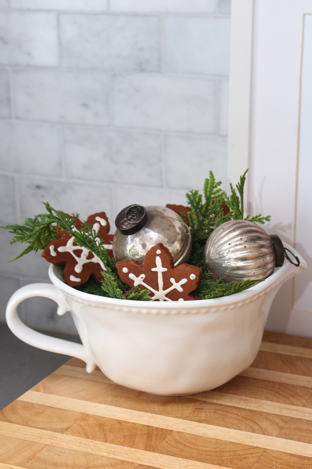 White kitchen bowl filled with greenery, ornaments, and faux gingerbread snowflakes.