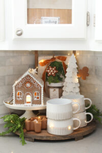 Round wood kitchen tray decorated with a lighted gingerbread house, mugs, and a tree for a cute Christmas display.