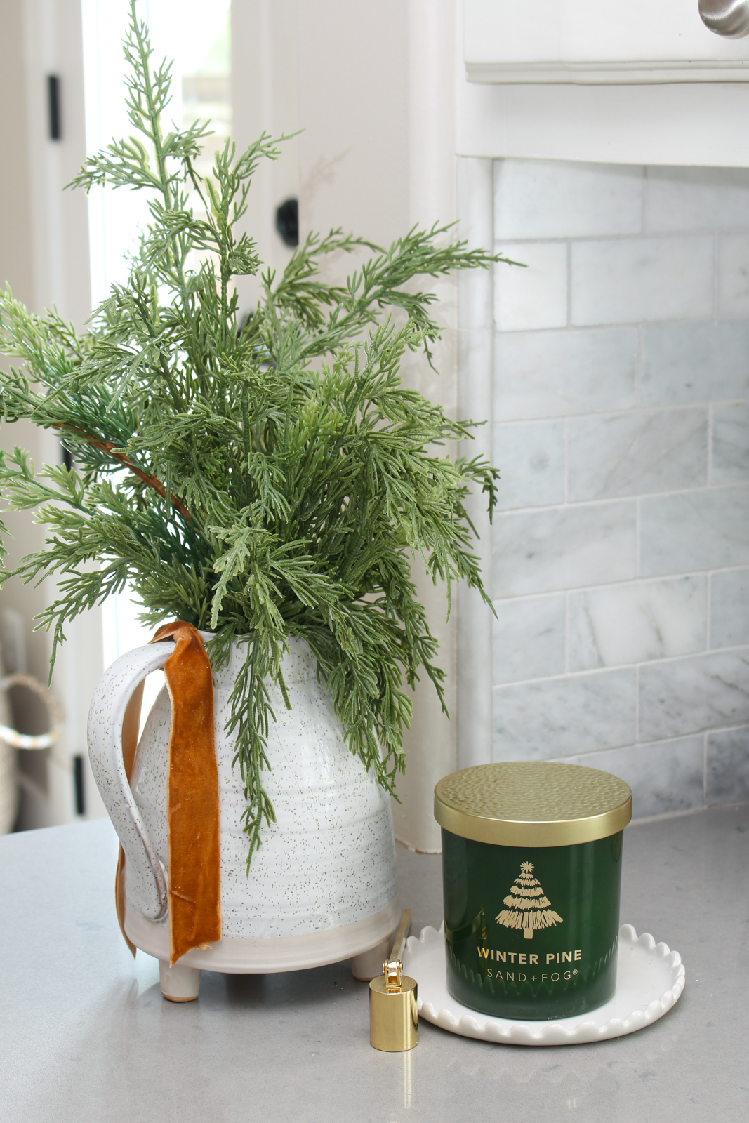 Christmas candle on a tray with a white jug filled with faux greenery.