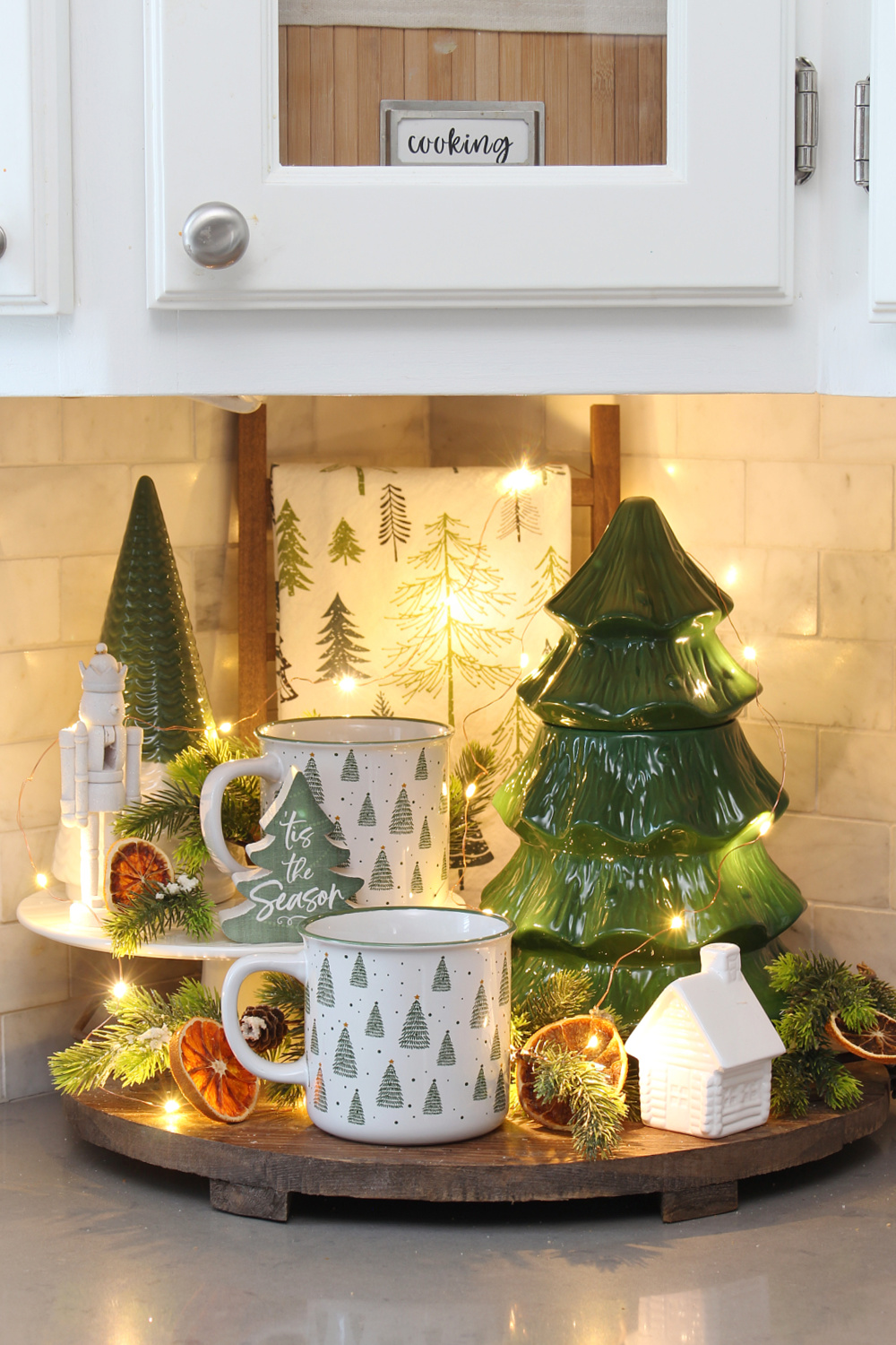 Wooden tray decorated for Christmas with green and white Christmas tree decor and twinkle lights.