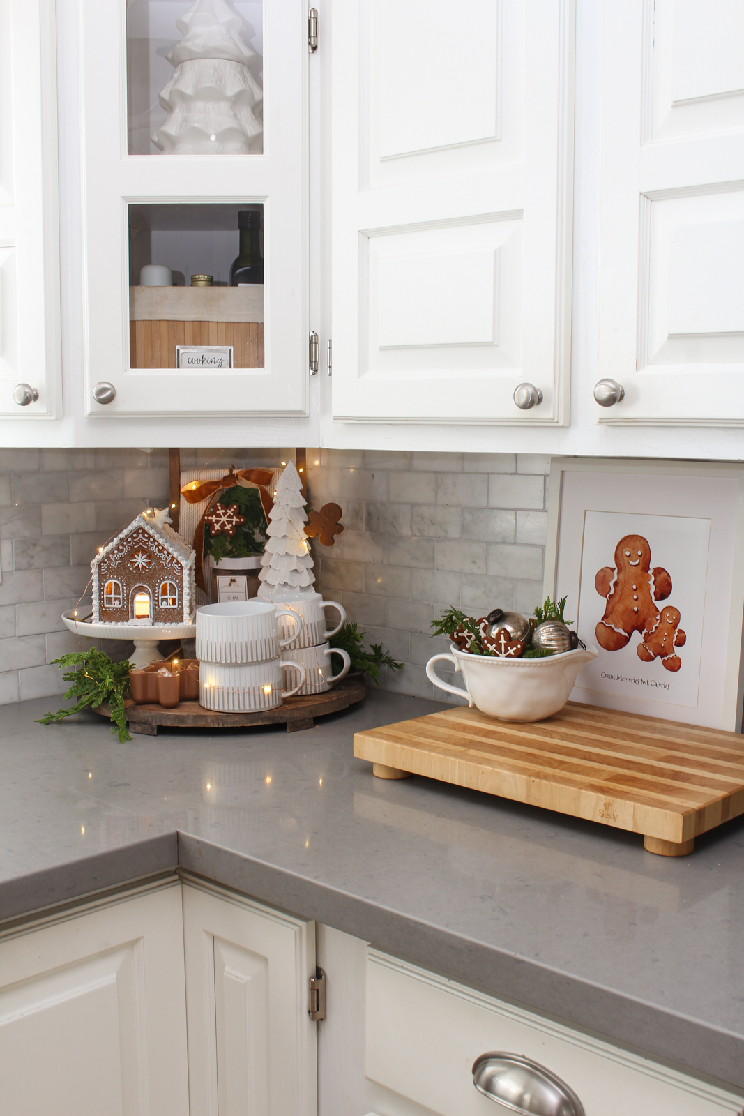 Round wood kitchen tray decorated with a lighted gingerbread house, mugs, and a tree for a cute Christmas display.