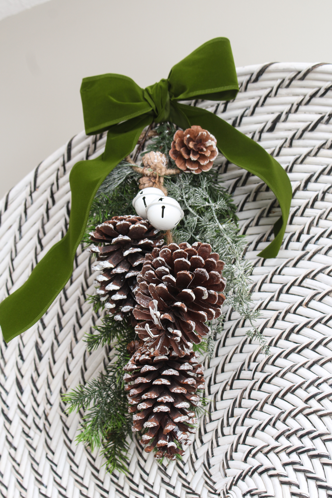 DIY Christmas swag made from greenery, pinecones, and green velvet ribbon. Hanging from a woven wall hanging basket.