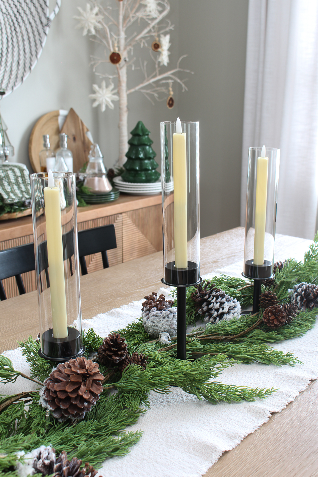 Christmas centerpiece using black candlesticks, faux greenery, snowy pinecones, and lights.