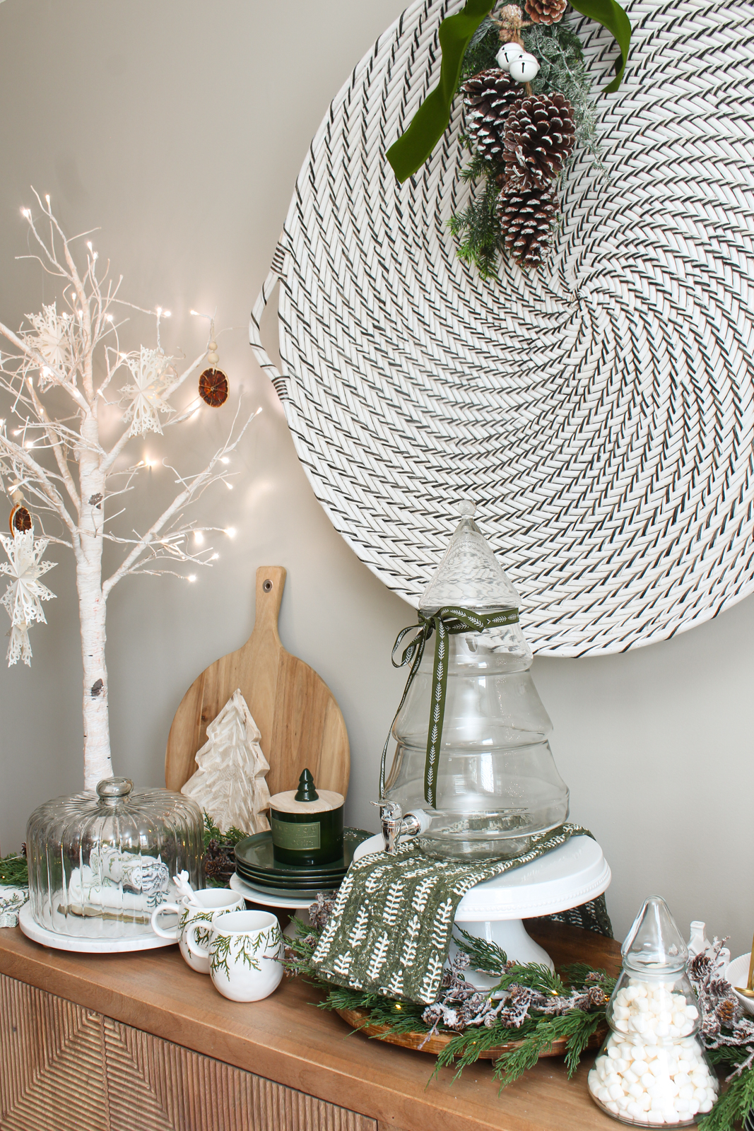 Glass tree beverage dispenser on a cake stand with green ribbon tied around it.