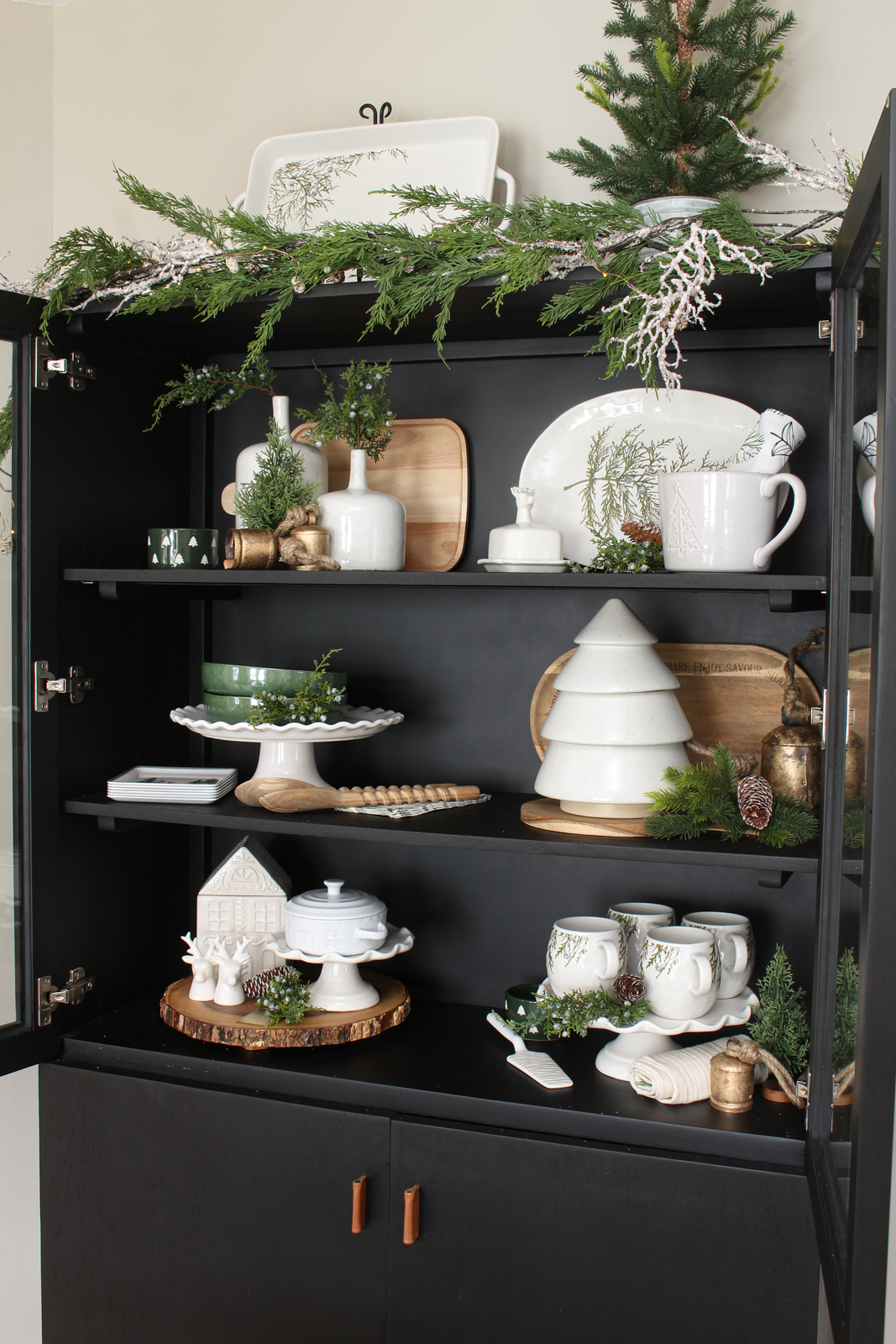 Black bar cabinet decorated for Christmas with white, forest green and wood decor pieces.