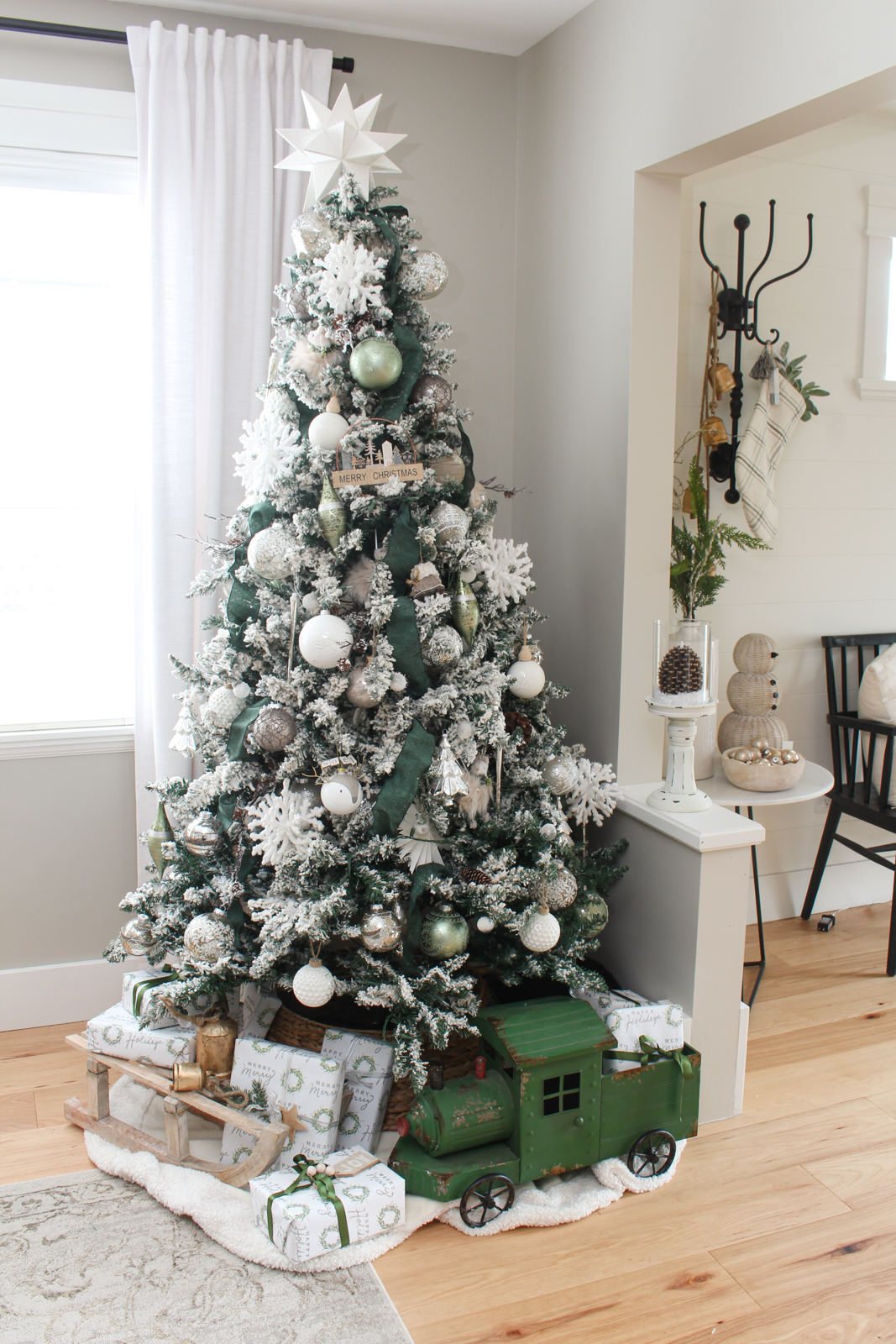 Christmas dining room Christmas tree decorated with a winter wonderland theme. Flocked tree is filled with green riboon, silver and white decorations, and woodsy touches just as branches and pinecones.