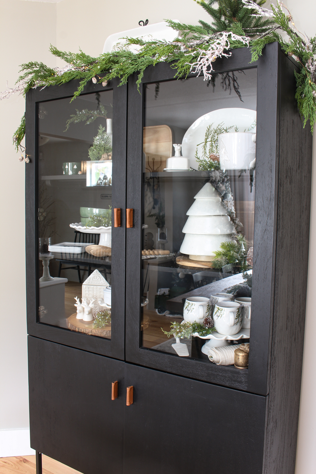 Black bar cabinet decorated for Christmas with white, forest green and wood decor pieces.