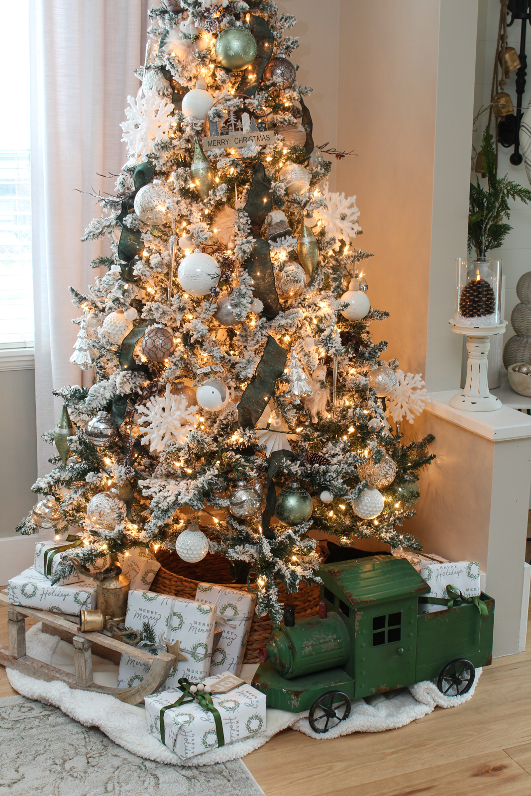 Christmas dining room Christmas tree decorated with a winter wonderland theme. Flocked tree is filled with green riboon, silver and white decorations, and woodsy touches just as branches and pinecones.