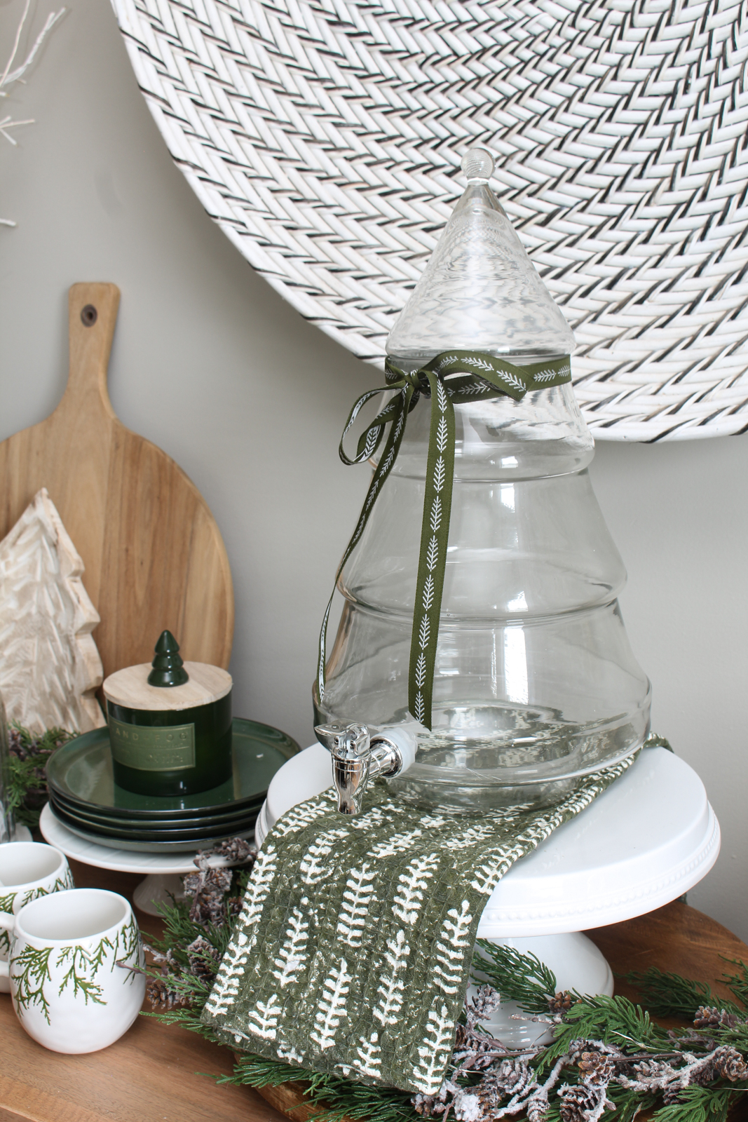 Glass tree beverage dispenser on a cake stand with green ribbon tied around it.