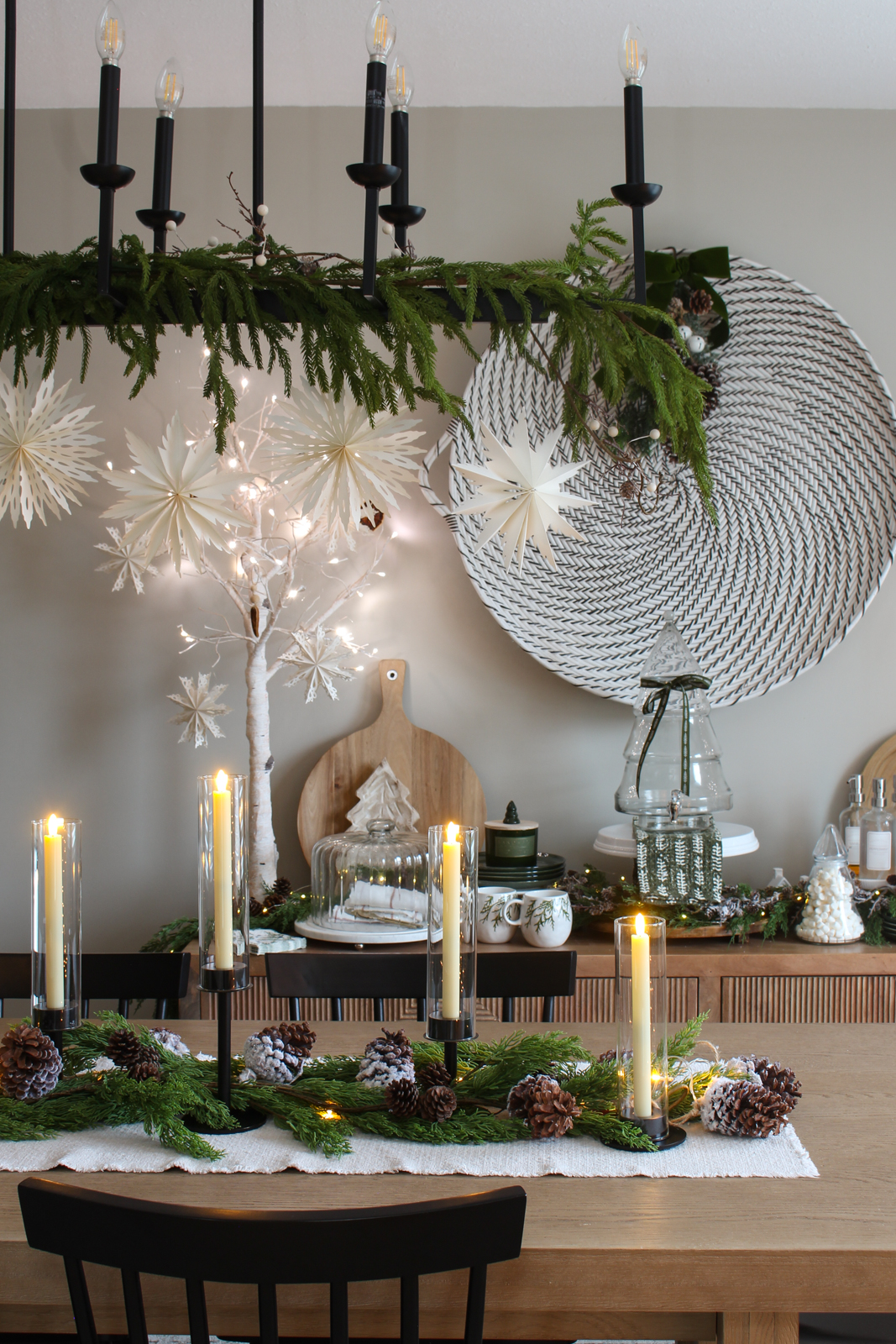 Christmas centerpiece using black candlesticks, faux greenery, snowy pinecones, and lights.