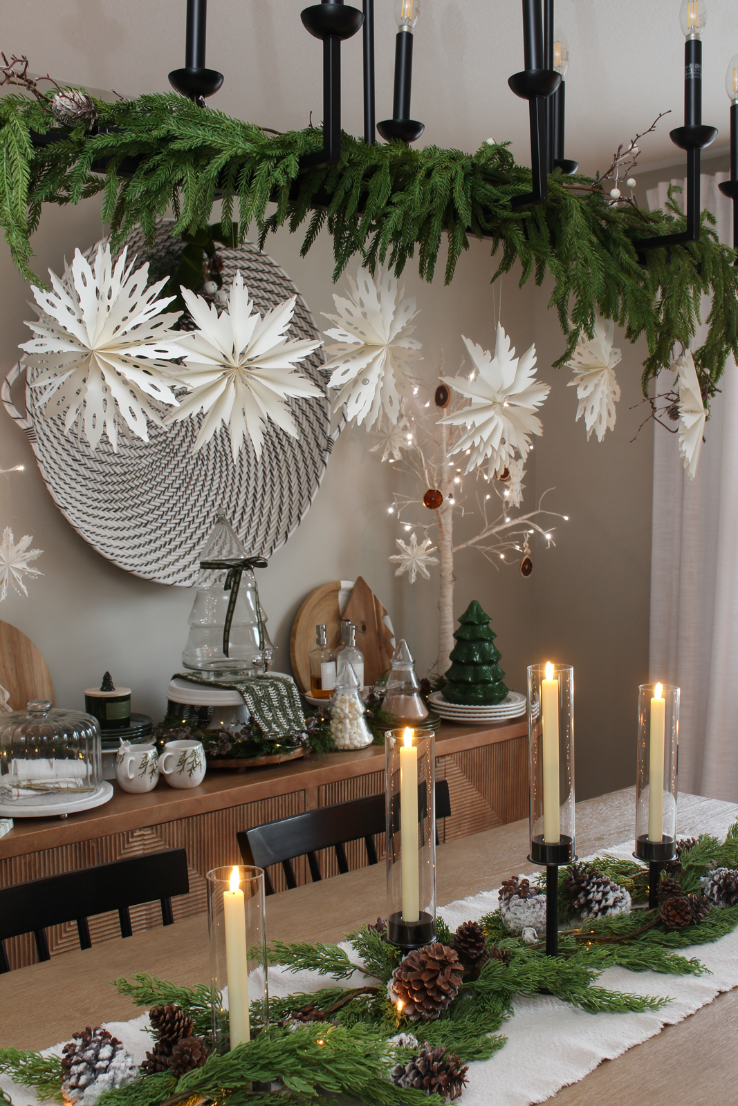 Christmas centerpiece using black candlesticks, faux greenery, snowy pinecones, and lights.